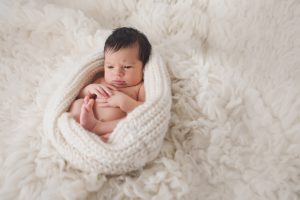 newborn baby awake eyes open cream flokati rug curled up pose